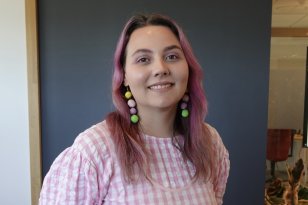 UX-designer Linn Karolina Rebnord Jente med rosa hår og rosa og hvit rutete kjole som smiler foran en vegg.