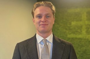 Mann med blondt hår, grå dress, hvit skjorte og slips som smiler til kamera.