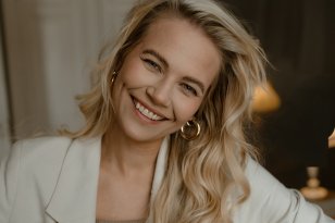 Fotograf Bethine Elizabeth Borresen Kvinne med langt lys hår smiler til kamera. Hun har på seg hvit blazer og beige topp.