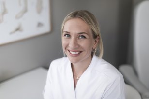 Ei dame med hestehale og hvit skjorte sitter foran en lys vegg