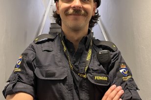 En ung mann i uniform står nederst i en trapp. Han holder armene foldet foran brystet. 