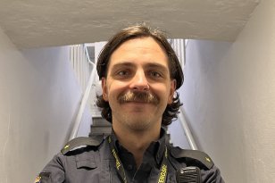 En ung mann i uniform står nederst i en trapp. Han holder armene foldet foran brystet. 