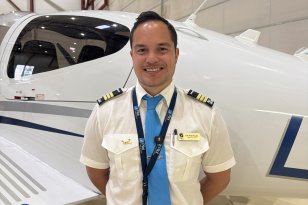 Flyinstruktør Erik Andre Raaket Mannlig flyinstruktør med hvit skjorte, blått slips og sort bukse smiler foran fly.