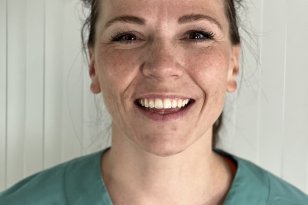 Kvinne med hestehale og grønn operasjonsuniform. Hun smiler og ser rett inn i kameraet.