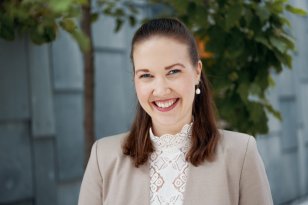 Kvinne med brunt hår, beige dressjakke, hvit bluse. Hun smiler til kameraet.