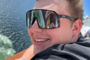 En mann med kort hår og solbriller og svart trøye med blå himmel bak.ak