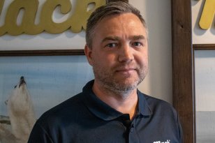 Markedssjef Ken Stian Olsen. Han har på seg blå t-skjorte. Han står foran et bilde med en isbjørn.