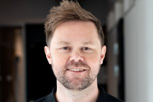 En mann i svart t-skjorte. Han smiler.