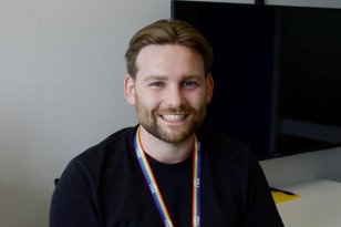 Mann med svart t-skjorte og brunt hår. Rund halsen har han en et nøkkelknippe med regnbuefarger. Mannen smiler til kamera.