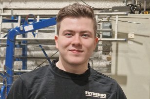 Mann med svart genser står i et verktsted og ser inn i kamera