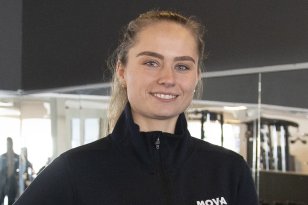 En kvinne i treningstøy. Hun smiler. Hun er på et treningssenter. 