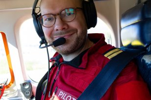 En mann i rød pilot-uniform. Han er i et fly.