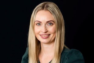 Smilende kvinne med blå øyne og langt lyst hår delt i midtskill.