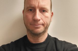 Mann med svart genser ser inn i kamera. Hvit bakgrunn. 
