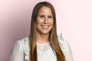 Portrettbilde av en dame med langt, mørkeblond hår og hvit topp. Bakgrunnen er lys rosa