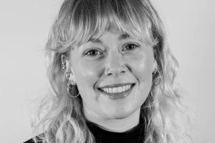 Et svart-hvitt portrettbilde av en jente med langt hår og som smiler til kamera
