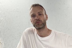 En mann i hvit t-skjort står foran en hvit vegg