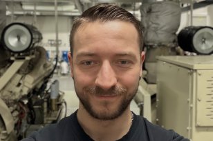 Mann med svart t-skjorte står i et kontrollrom på en båt