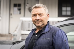 Mann i mørk vest og blå skjorte. Han ser rett i kameraet. Han er ute.