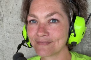 En dame med mørkt hår og gule øreklokker står foran en grå vegg.