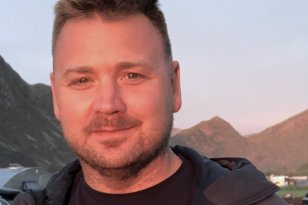 Mann med svart genser og jakke og brunt hår ser inn i kamera