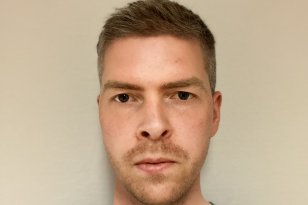 Patolog Eirik Storebø En mann med grønn legeskjorte med lyst hår og skjegg. Bakgrunnen er en lys vegg.