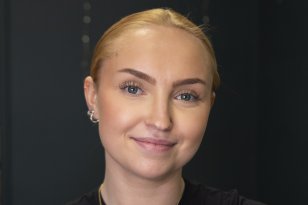 En dame med blondt hår og svart genser. Hun ser rett i kameraet.