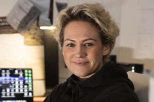 En dame med blondt hår og svart genser. Hun ser rett i kameraet.