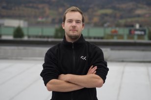 Kuldeteknikeren står med armene i kors og ser inn i kamera, mens han står på et flatt tak. Han har på seg en svart fleecejakke med en firmalogo "GK" på brystet. 