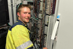 Maritim elektriker Arne Johan Svendsby foran brann og gass-kabinettet Mann med lyst hår sitter foran kabinett med mange ledninger. Han har gul arbeidsjakke på.