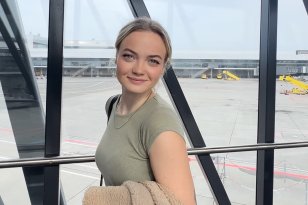 Lettmatros Hedda Othilie Hildre Dame med lysegrønn t-skjorte og lyst hår i hestehale står i en gang med glassvegger på en flyplass