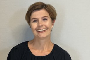 Reiselivsmedarbeider Helen Granlund En kvinne med kort, lysebrunt hår smiler mot kameraet. Hun har på seg en mørk, langermet bluse og står foran en lys, ensfarget vegg.