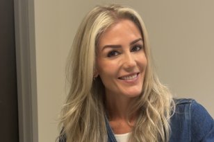 Kvinne med langt blondt hår smiler til kamera. Hun har på seg en mørkeblå dongeri­jakke, med en hvit T-skjorte synlig under.