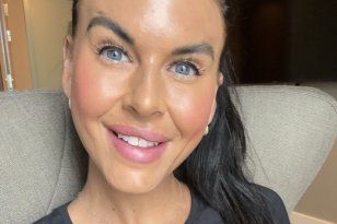 En dame i svart genser smiler til kamera. Hun har blå øyne, brunt hår og håret er i hestehale. Hun sitter i en grå sofa og bak hun er det en svart TV på veggen. 