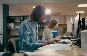 En mann og en kvinne jobber med foran datamaskiner i et kontorlandskap