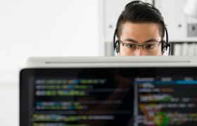 En mann sitter bak en pc-skjerm det det står noe kode