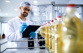 Mann med labfrakk og hårbånd følger med på produksjon av matolje