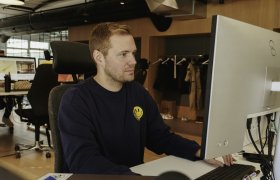 En mann i svart genser sitter foran en dataskjerm