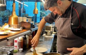 Mann i med skjegg i svarte kokkeklær legger opp pasta på en tallerken