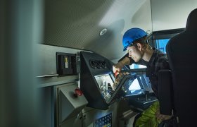 En person i et teknisk rom reparerer ledninger. Personen har blå hjelm og arbeidsklær.