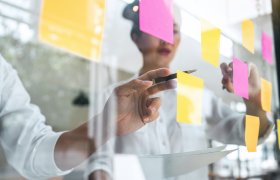 To personer henger opp post-its i ulike farger på en glassvegg. 