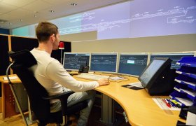 En togleder sitter bak et skrivebord og ser på skjermer med bilder av togspor