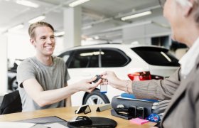 Bilselger overleverer nøkler til kjøper av ny bil. 