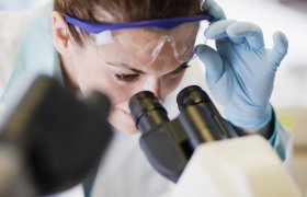 Patolog titter inn i mikroskop.