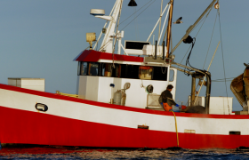 En rød fiskebåt til havs med en person ombord.