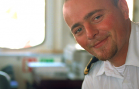 En styrmann i uniform jobber med navigering inne på dekk.  