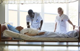 Mannlig sykepleier undersøker pasient mens kvinnelig sykepleier står ved siden av og ser på.