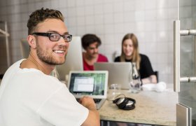 Webdesigner foran dataskjerm med kolleger i bakgrunnen.