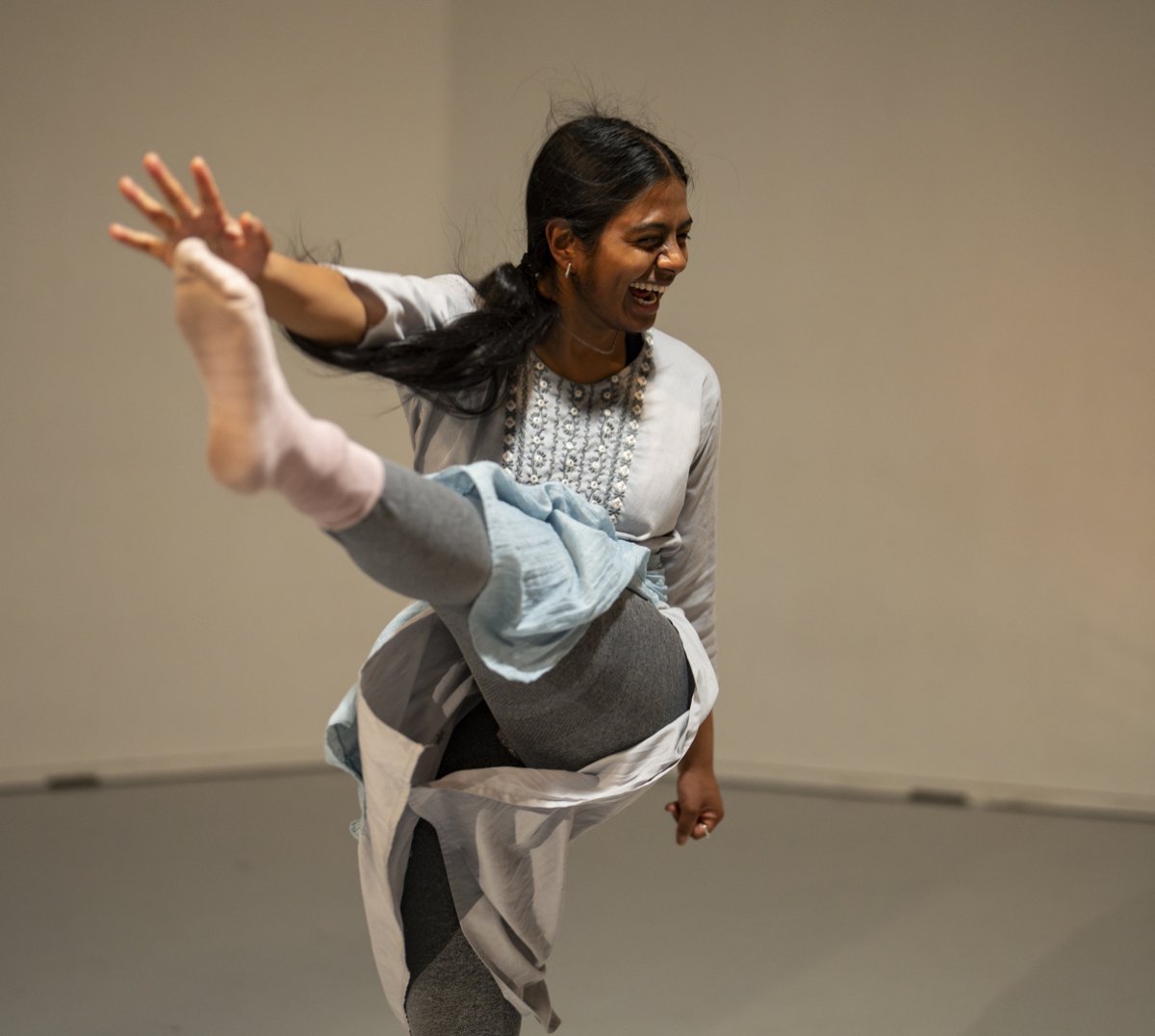 En person danser og smiler med foten og armen opp i været.