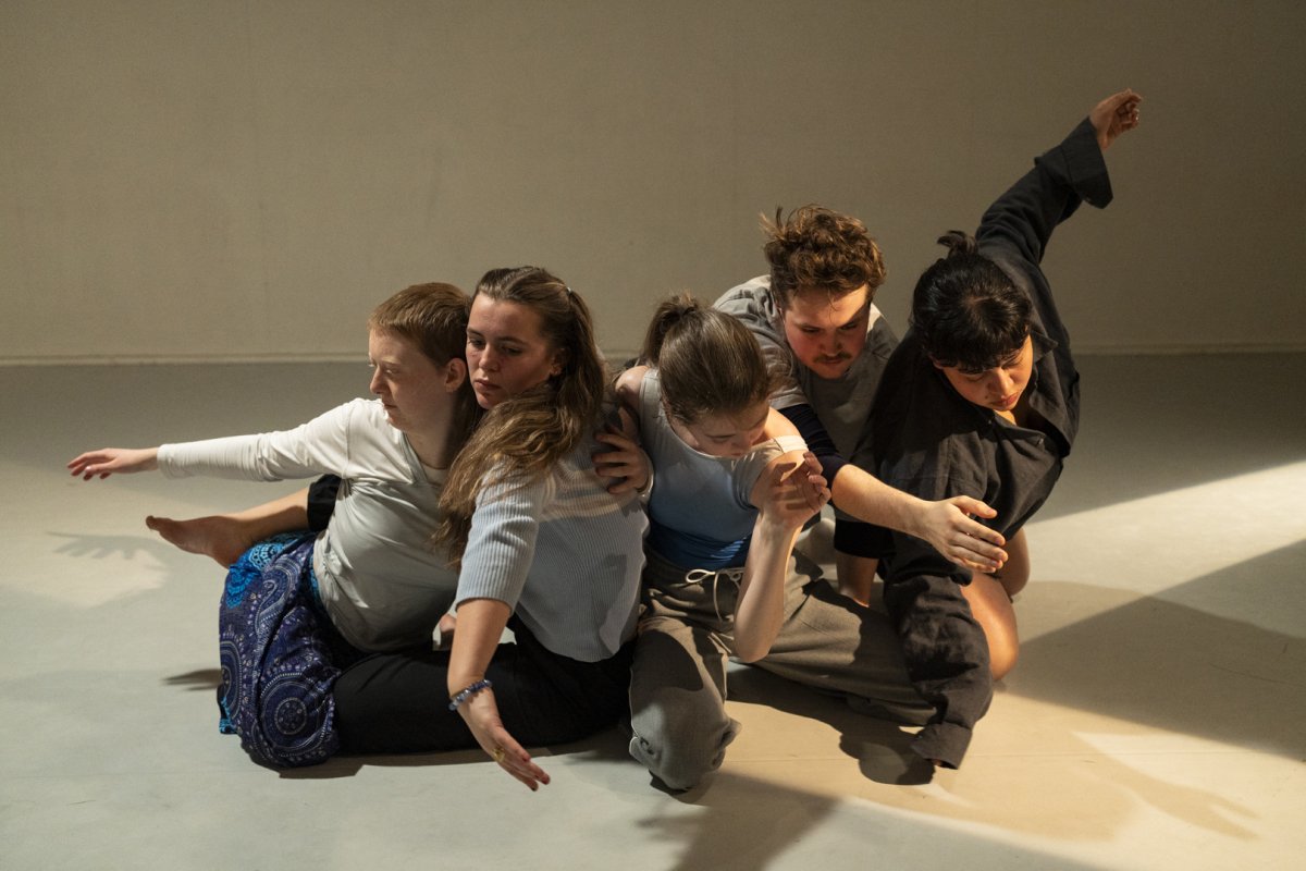 Fem personer danser i en klump på bakken med armene i ulike retninger.